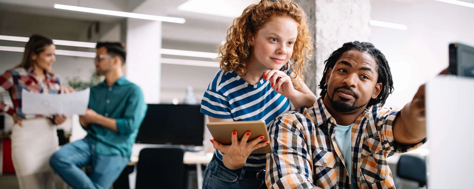 A photo of a man in front of a computer pointing at something and showing the girl beside him.